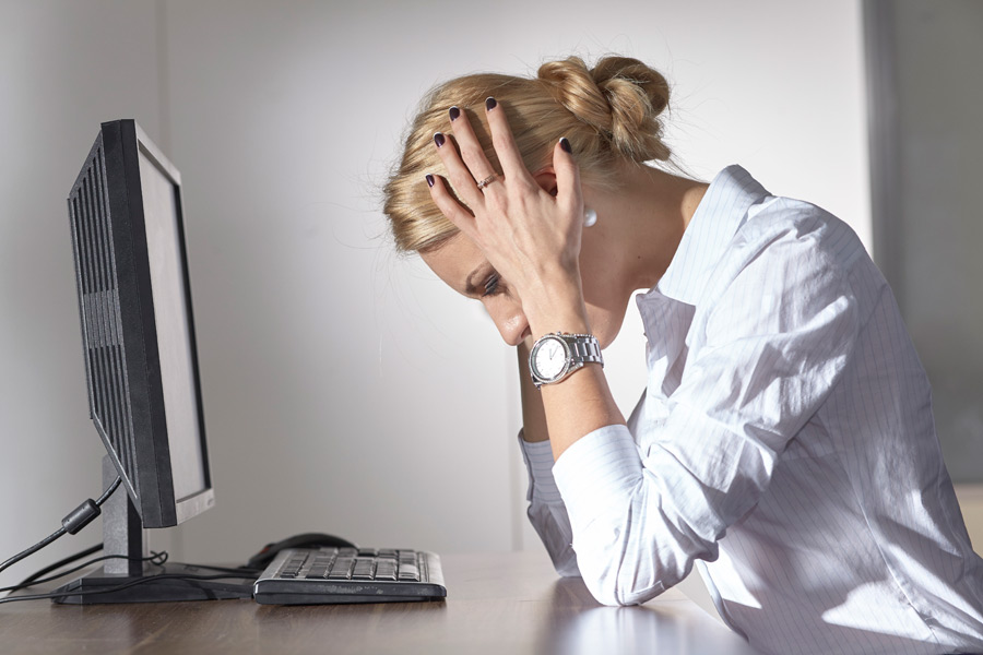 ネット回線の不調に悩む女性|通信トラブルのイメージ パソコンの前でネット回線の不調に頭を抱えて悩む女性の様子